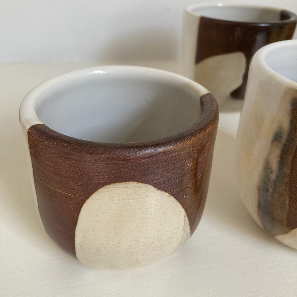 Handmade tumbler with dark glaze and a pale drip, white interior
